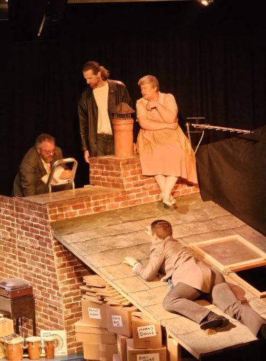 4 people on a roof - one sitting, one standing, one on a ladder and one clinging on